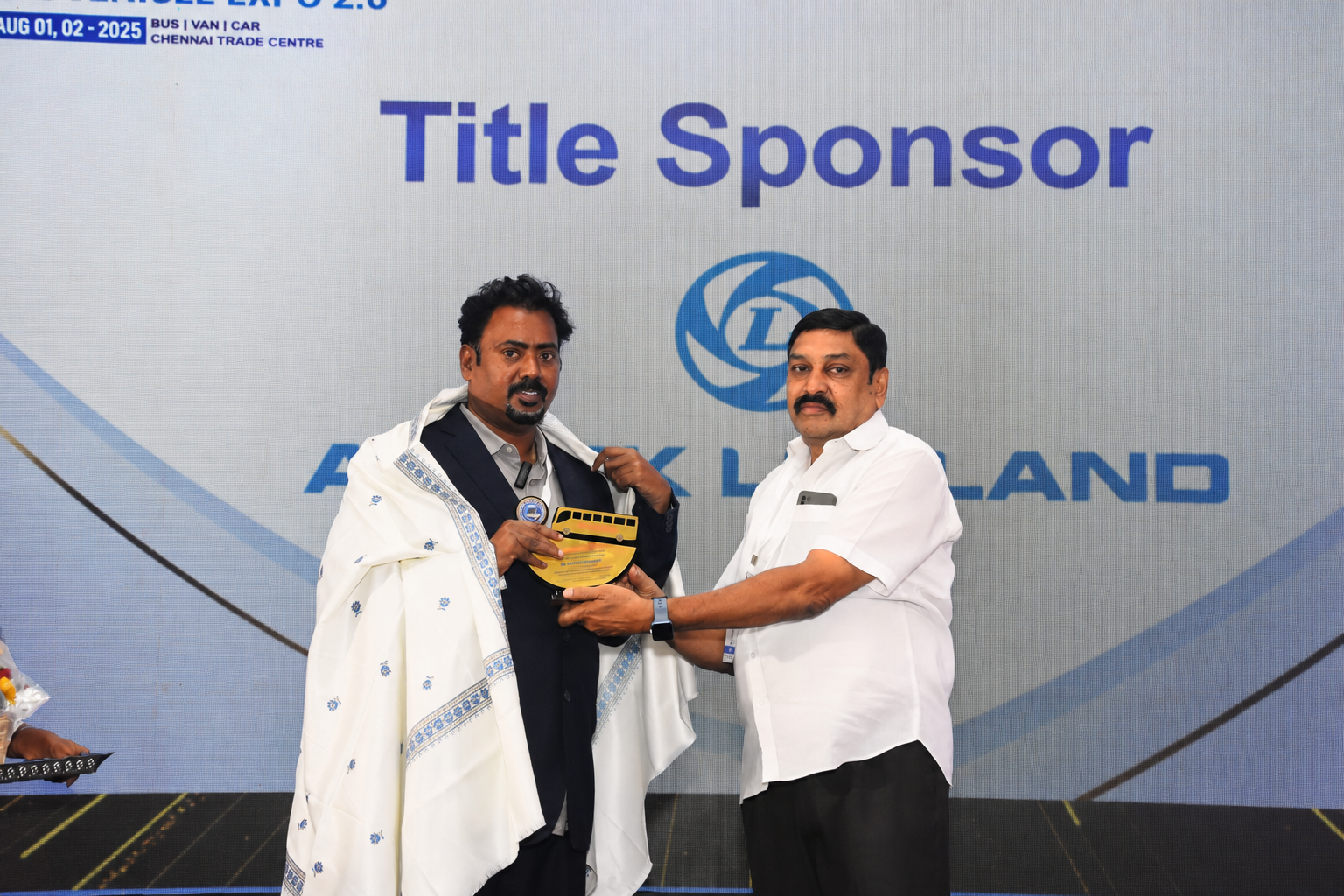 Dr. V. Amudhan being honoured with a shawl at the Ashok Leyland Title Sponsor booth